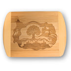 A premium engraved bamboo cutting board featuring "The Roots" local illustration of the Agate Pass Bridge, a Washington State Ferry, and a Great Blue Heron bird, handcrafted by The Blended Oasis in Suquamish, Washington.