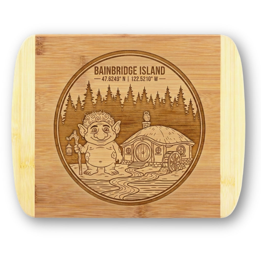 A premium engraved bamboo cutting board featuring "The Island Troll" emblem showcasing a friendly troll with a lantern, a hobbit house with a waterwheel, and Bainbridge Island coordinates, handcrafted by The Blended Oasis.
