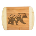 A premium engraved bamboo cutting board featuring an intricate illustration of a grizzly bear silhouette filled with mountains, evergreen trees, and flying eagles, handcrafted by The Blended Oasis in Washington State.