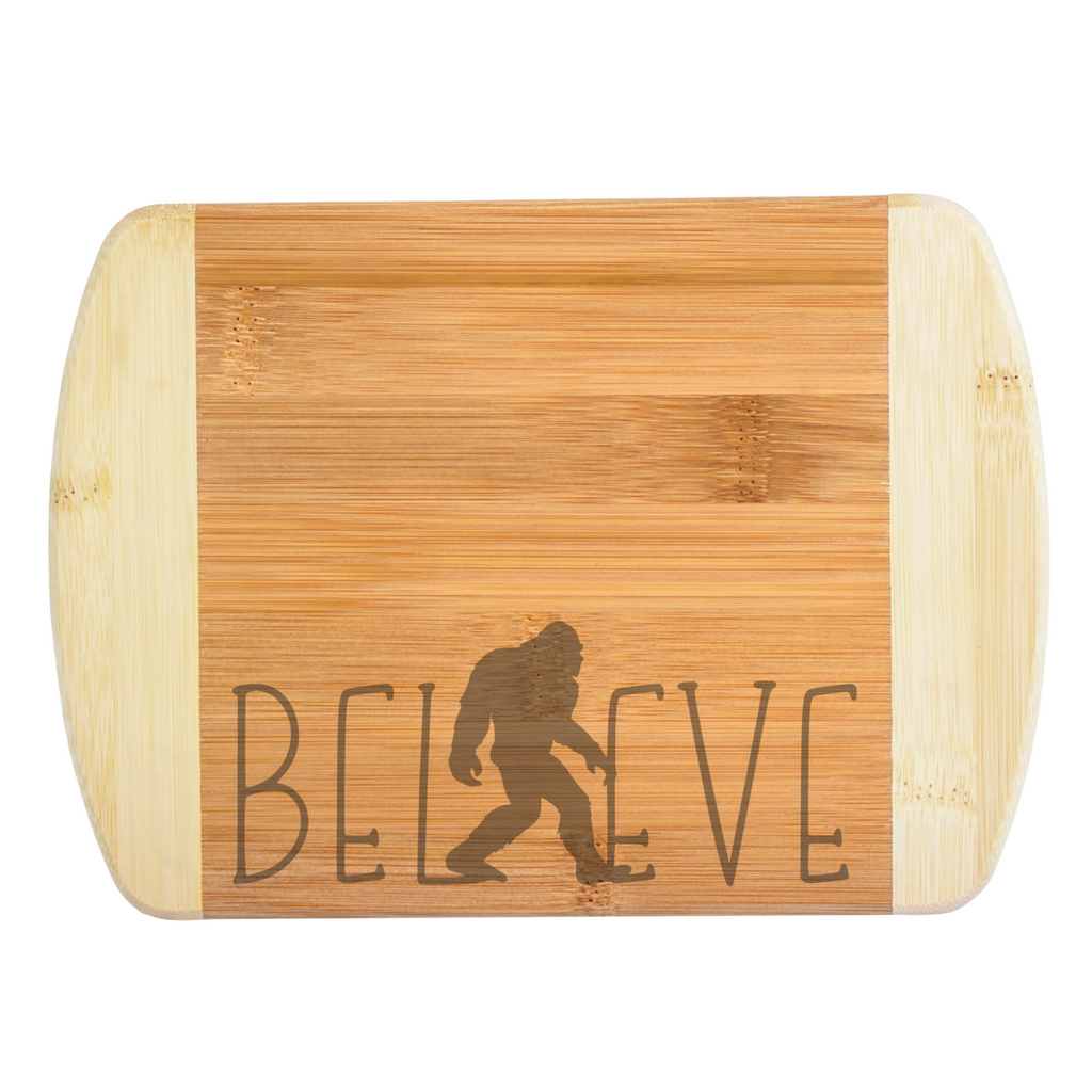 A premium engraved bamboo cutting board featuring a modern handwritten text design that reads Believe, with a walking Bigfoot silhouette serving as the letter I, handcrafted by The Blended Oasis in Washington State.