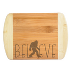 A premium engraved bamboo cutting board featuring a modern handwritten text design that reads Believe, with a walking Bigfoot silhouette serving as the letter I, handcrafted by The Blended Oasis in Washington State.