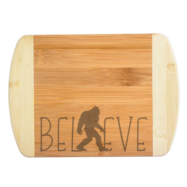 A premium engraved bamboo cutting board featuring a modern handwritten text design that reads Believe, with a walking Bigfoot silhouette serving as the letter I, handcrafted by The Blended Oasis in Washington State.