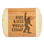 A premium engraved bamboo cutting board featuring a funny illustration of Bigfoot throwing a peace sign next to bold text that reads Hide and Seek World Champ, handcrafted by The Blended Oasis in Washington State.