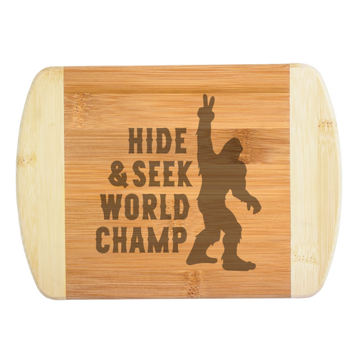 A premium engraved bamboo cutting board featuring a funny illustration of Bigfoot throwing a peace sign next to bold text that reads Hide and Seek World Champ, handcrafted by The Blended Oasis in Washington State.