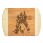 A premium engraved bamboo cutting board featuring an intricate illustration of a giant footprint framed by pine trees and filled with a crescent moon, starry night sky, mountains, and a walking Bigfoot silhouette, handcrafted by The Blended Oasis in Washington State.