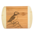 A premium engraved bamboo cutting board showcasing a detailed illustration of a puffin bird standing on a rocky coastal cliff, handcrafted by The Blended Oasis in Washington State.