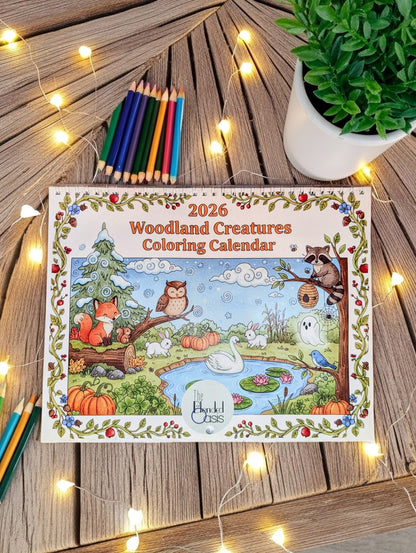2026 Woodland Creatures Coloring Calendar on a wooden surface with coloring pencils and a plant.