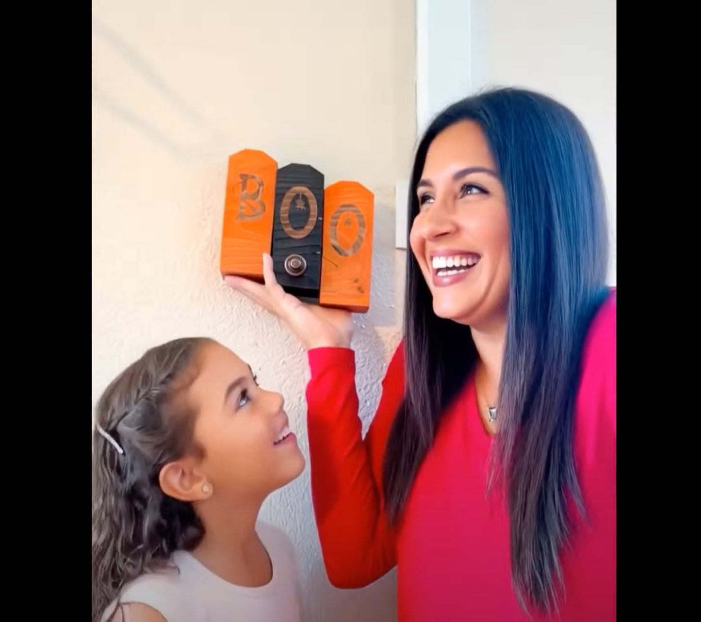 Woman and child holding up 'BOO' candy containers against a white wall
