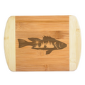 A rustic laser-engraved bamboo cutting board featuring a unique hybrid design of a fish silhouette filled with a detailed lakeside wilderness scene, a fisherman in a kayak, and a rising sun, handcrafted by The Blended Oasis in Washington State.