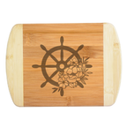 An elegant laser-engraved bamboo cutting board featuring a detailed nautical ship wheel accented with a beautiful bouquet of blooming flowers, handcrafted by The Blended Oasis in Washington State.
