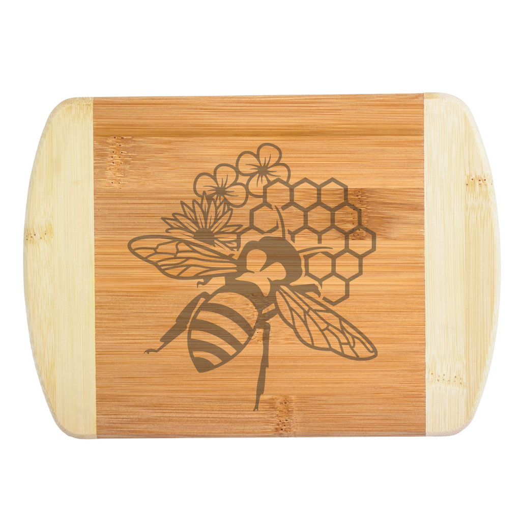 A premium engraved bamboo cutting board featuring a unique honeybee design layered with geometric honeycomb shapes and garden flowers, handcrafted by The Blended Oasis in Washington State.
