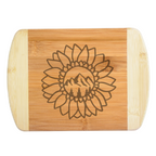 A beautiful laser-engraved bamboo cutting board featuring a unique hybrid design of a blooming sunflower with mountains and pine trees in the center, handcrafted by The Blended Oasis in Washington State.