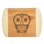 A premium engraved bamboo cutting board featuring a cute, whimsical modern illustration of a stylized owl with large round eyes, handcrafted by The Blended Oasis in Washington State.