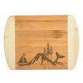 A premium engraved bamboo cutting board featuring a unique baseline illustration collage of a sailboat, mountain peak, evergreen pine trees, and a whale tail fluke, handcrafted by The Blended Oasis in Washington State.