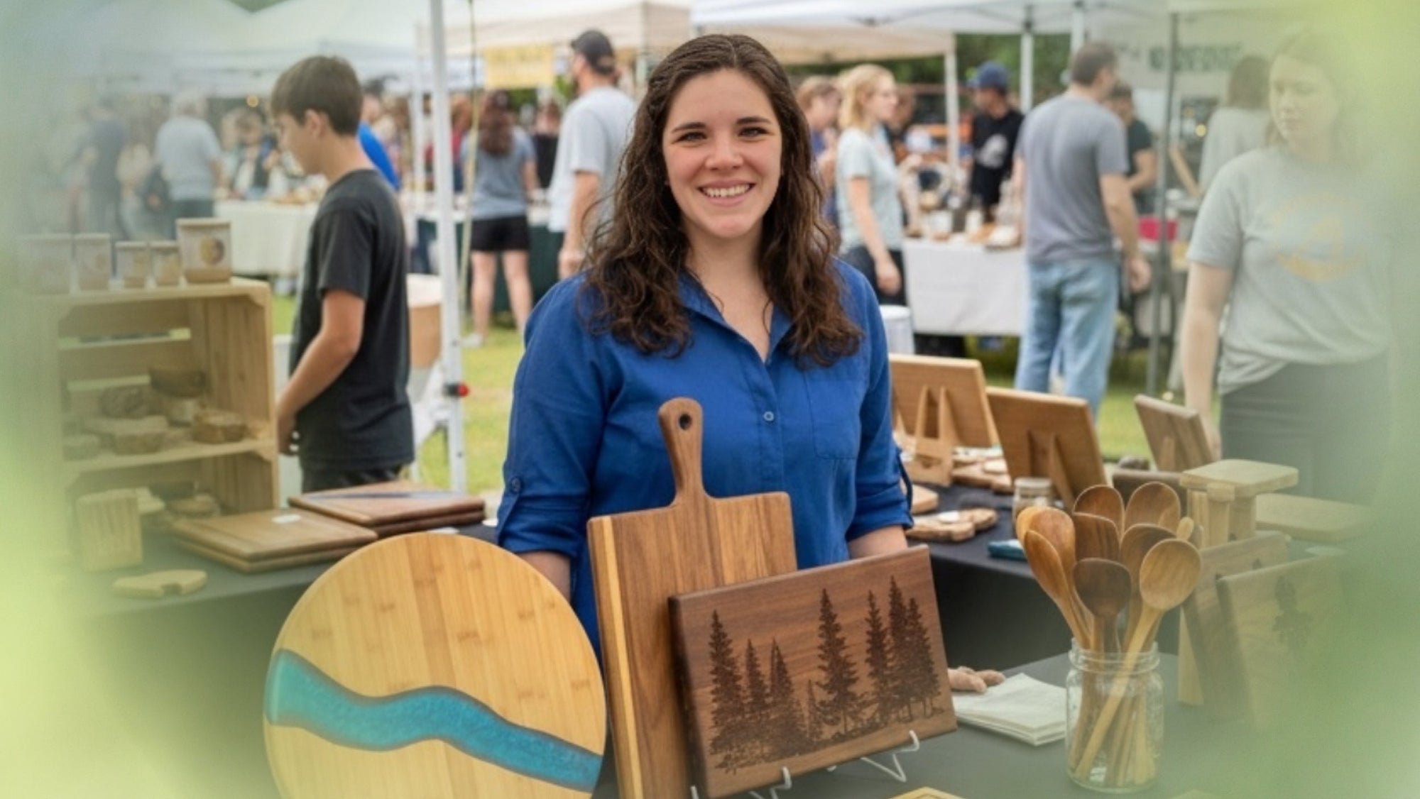 Woman standing behind a table displaying wooden products at an outdoor market.