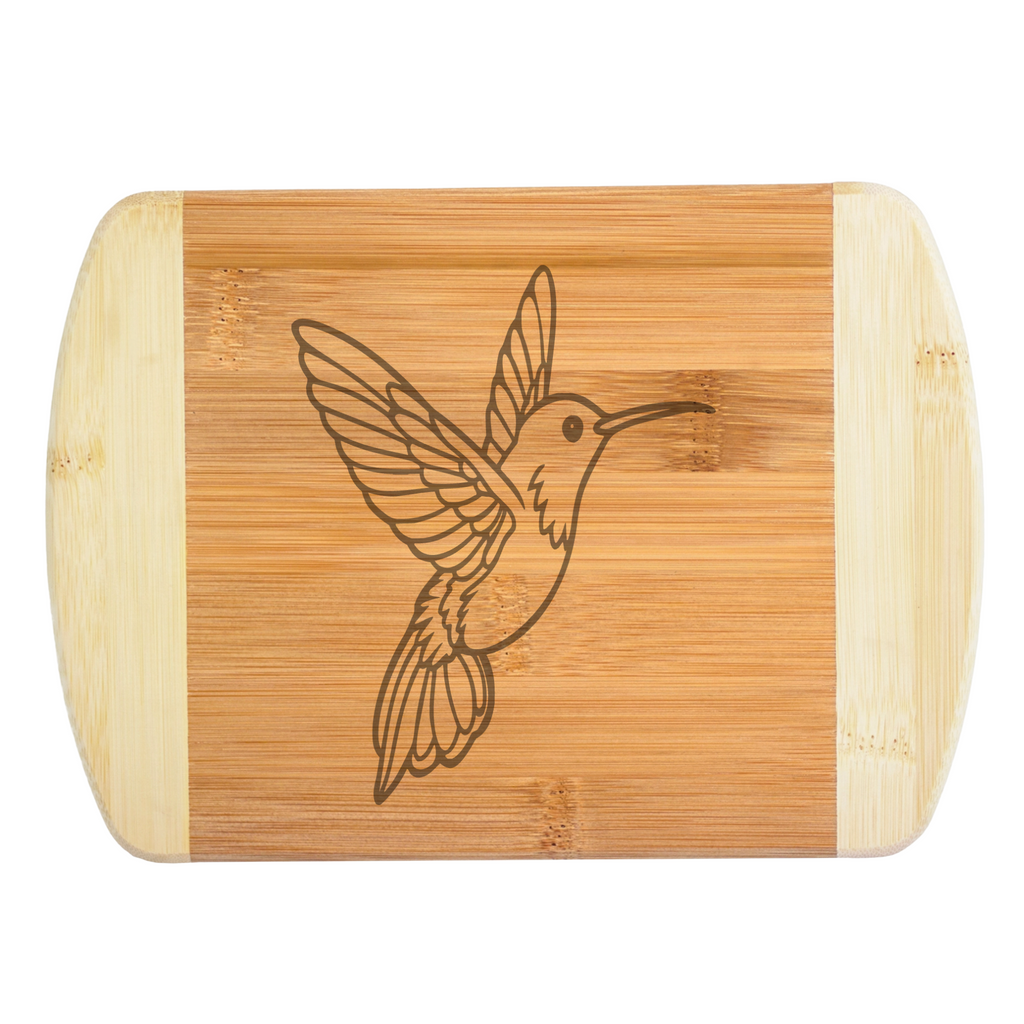 A premium engraved bamboo cutting board featuring a detailed design of a soaring hummingbird with outstretched wings, handcrafted by The Blended Oasis in Washington State.