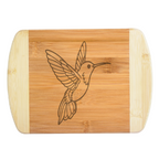 A premium engraved bamboo cutting board featuring a detailed design of a soaring hummingbird with outstretched wings, handcrafted by The Blended Oasis in Washington State.