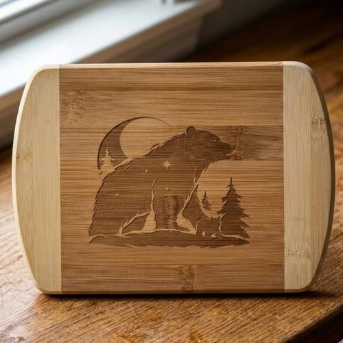 An artisanal serving board by The Blended Oasis showing an intricate laser etching of a large bear silhouette filled with a starry night sky, a crescent moon, and a tiny cub walking beside a pine tree. Shown in a close-up product shot on a rustic wooden table.