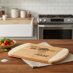 A humorous bamboo cutting board by The Blended Oasis featuring a laser engraving of a jellyfish alongside the playful text "Don't Be Jelly." The board rests on a rich wood counter next to a bowl of fresh tomatoes and a pinch of sea salt, with a kitchen stove in the background.