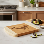 A sleek bamboo cutting board by The Blended Oasis featuring a large, detailed laser engraving of a humpback whale. Displayed on a bright marble countertop next to fresh avocados and a lime peel.