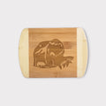A rectangular bamboo cutting board with rounded corners and handles, featuring a laser-engraved graphic of a bear and a fish in the center, shown against a light gray background.
