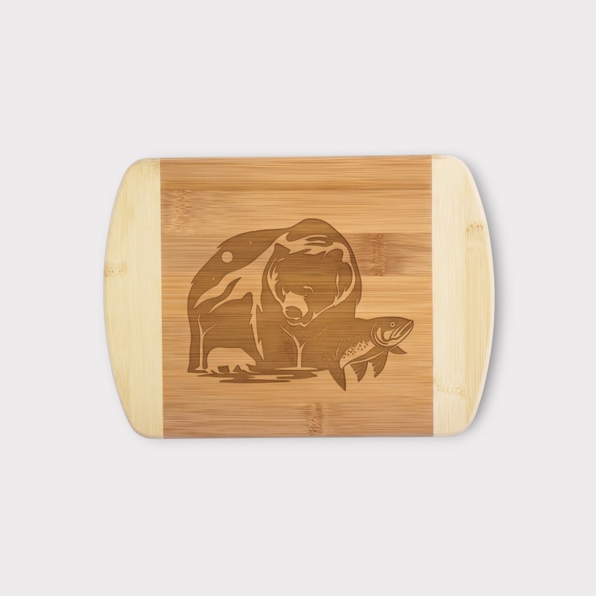 A rectangular bamboo cutting board with rounded corners and handles, featuring a laser-engraved graphic of a bear and a fish in the center, shown against a light gray background.