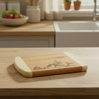 A premium bamboo charcuterie board from The Blended Oasis featuring a custom laser-engraved skyline of a sailboat, evergreen trees, a whale tail, and Mount Rainier. Displayed on a wooden countertop next to a white farmhouse sink.