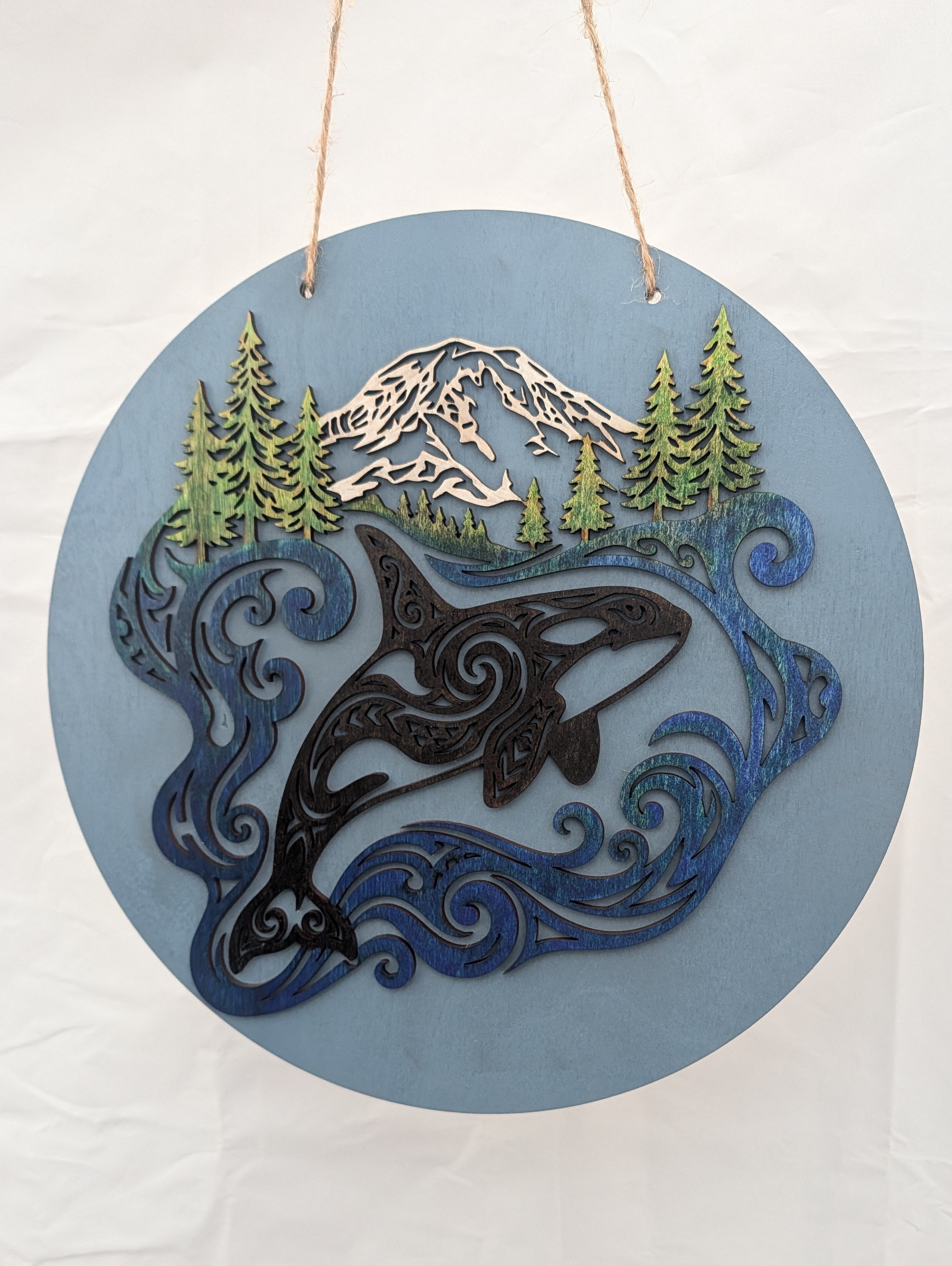 Decorative wall hanging with an orca whale, mountains, and trees on a blue background.