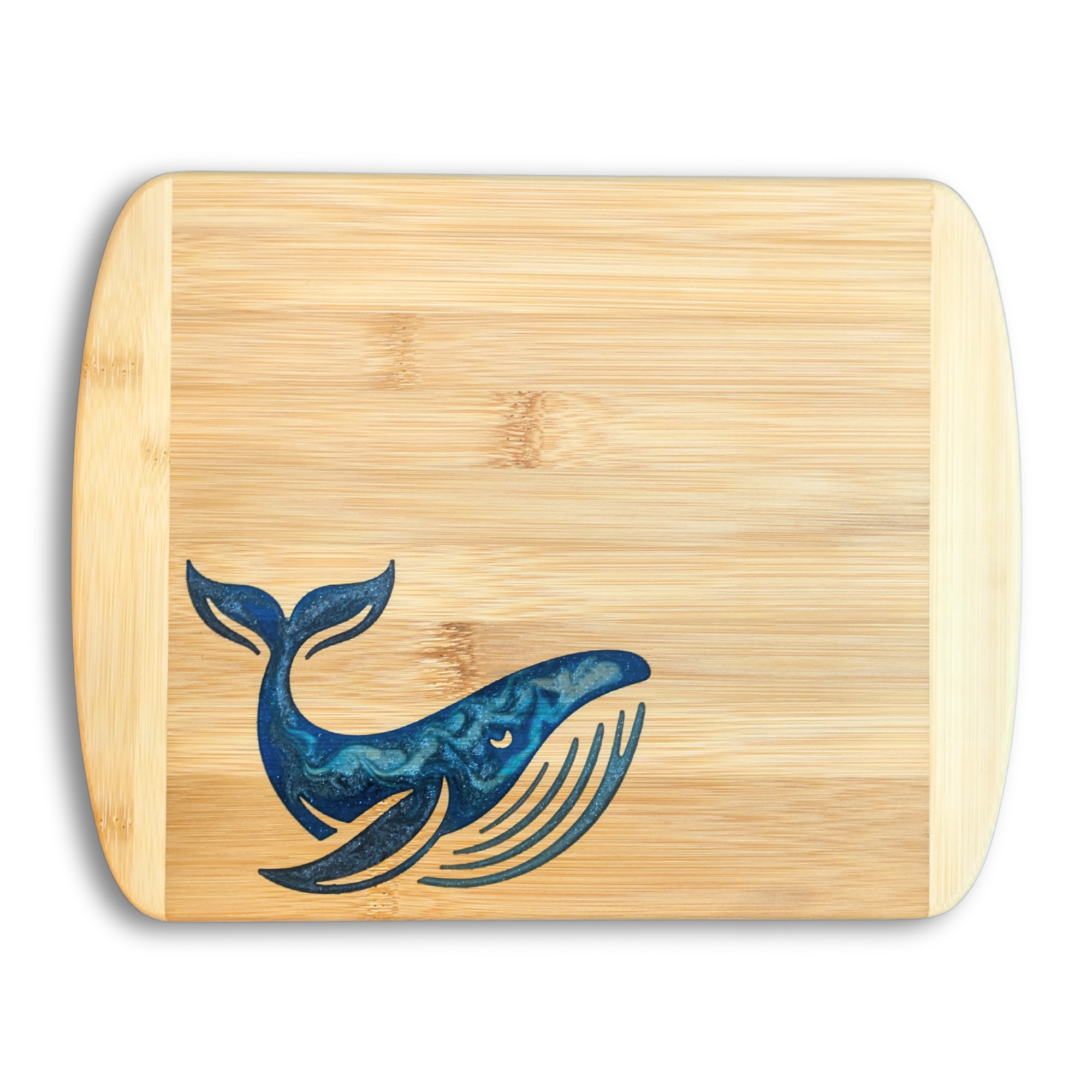 A top-down studio product photo by The Blended Oasis in Suquamish, WA, showing a handcrafted bamboo cutting board with a detailed epoxy resin inlay of a stylized blue baleen whale near the bottom edge. The resin features an intricate swirl of metallic royal blue and ocean teal tones. Set cleanly against a solid white background with a soft drop shadow.