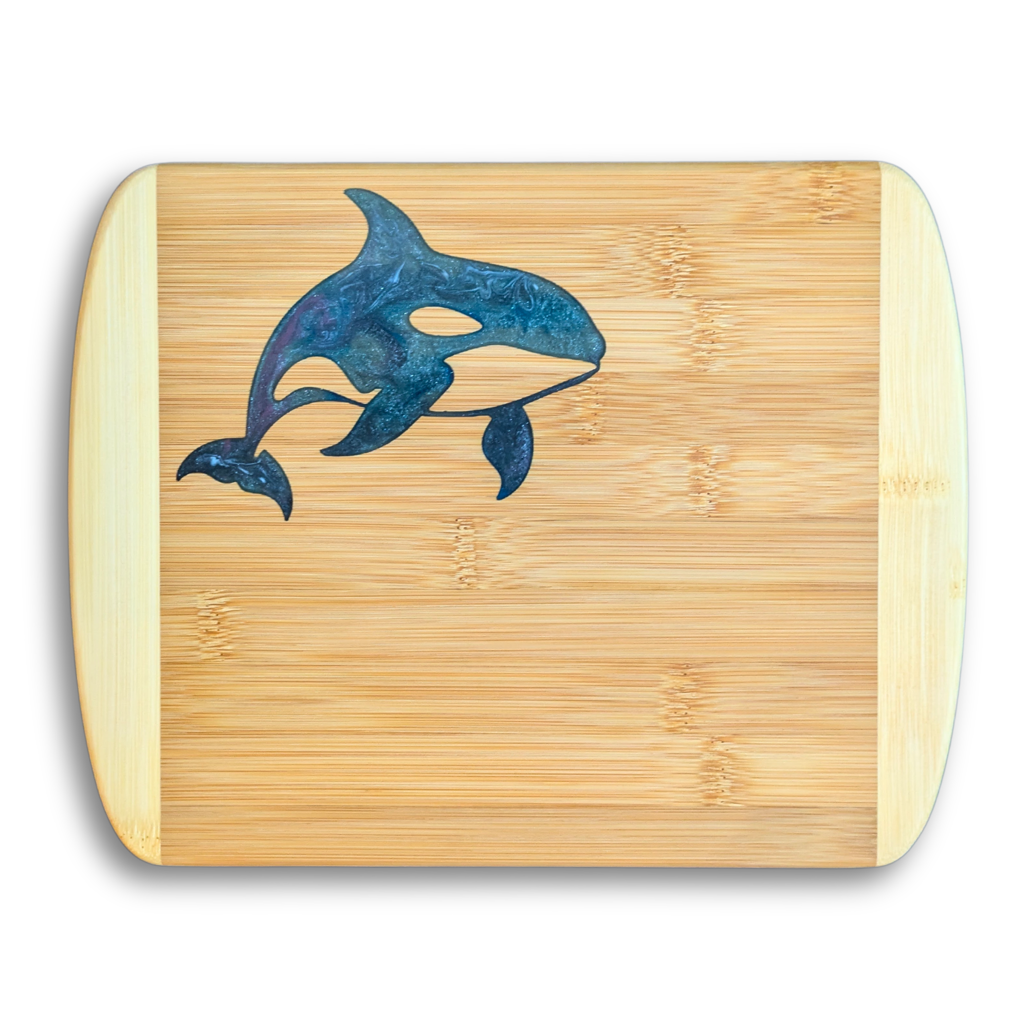 A crisp, top-down product photo by The Blended Oasis in Suquamish, WA, showing a handcrafted bamboo serving board featuring a second style variation of a breaching orca killer whale. The custom epoxy resin inlay features a lighter, shimmering ocean swirl of teal, silver-blue, and dark accents. Set on a solid white background with a clean drop shadow.