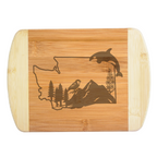 A premium engraved bamboo cutting board featuring an intricate design of Washington State filled with mountains, evergreen trees, a sparrow, a wildflower, and a leaping orca whale, handcrafted by The Blended Oasis in Washington State.