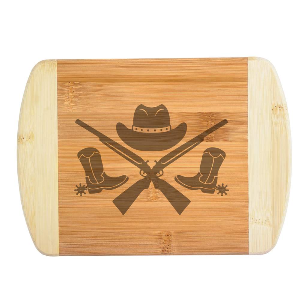 Close-up view of a custom laser-engraved bamboo cutting board featuring a detailed Western design with spurred boots, crossed rifles, and a cowboy hat, created by The Blended Oasis in Washington State.