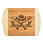 Close-up view of a custom laser-engraved bamboo cutting board featuring a detailed Western design with spurred boots, crossed rifles, and a cowboy hat, created by The Blended Oasis in Washington State.